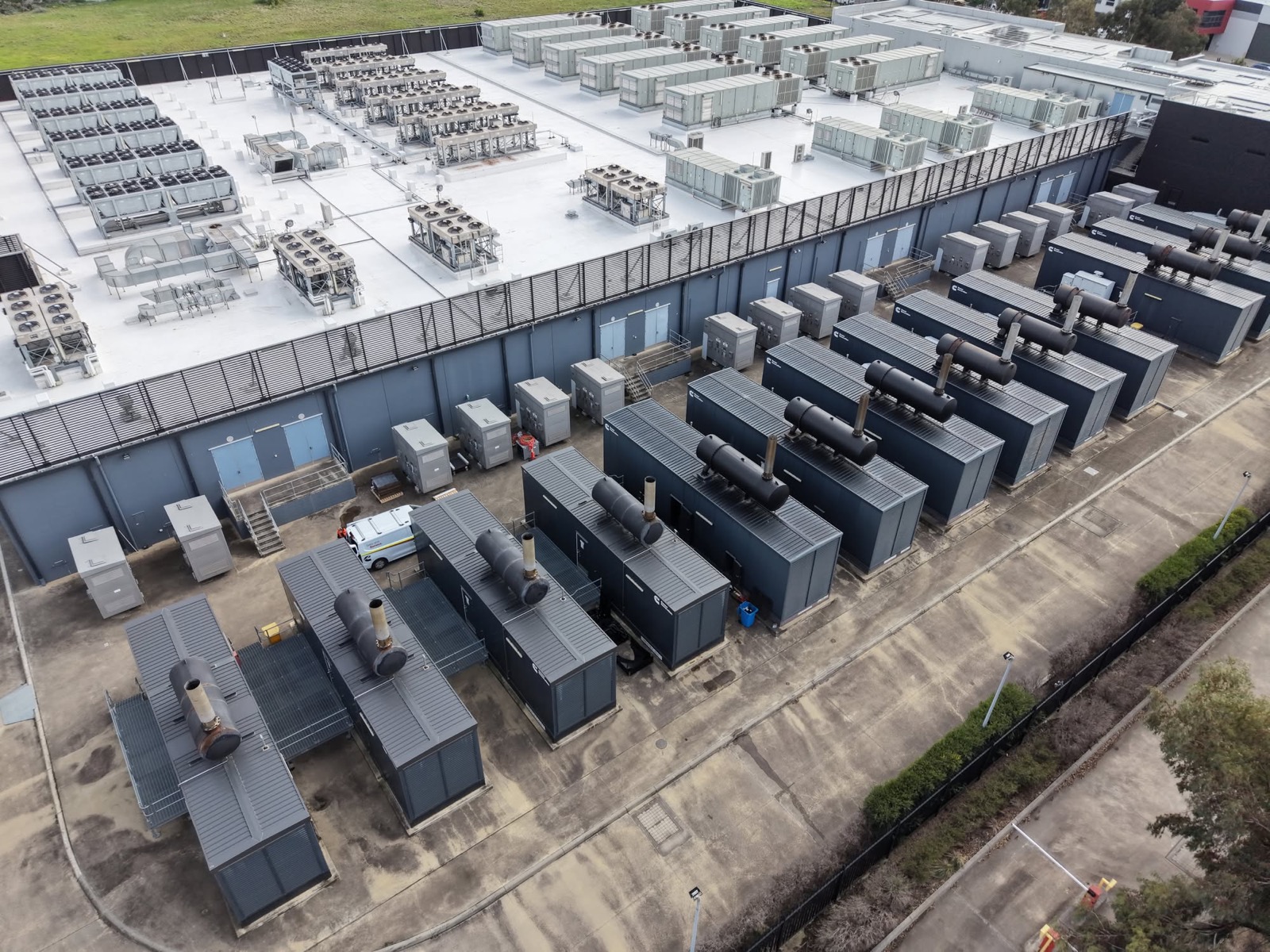 Aerial view of a data center, its roof covered with cooling units and rows of diesel backup generators lining the outside wall.
